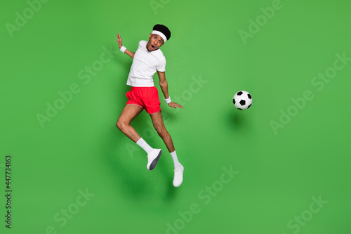 Fototapeta Naklejka Na Ścianę i Meble -  Photo of team player guy jump carefree kick soccer ball wear white t-shirt shorts sneakers isolated green color background