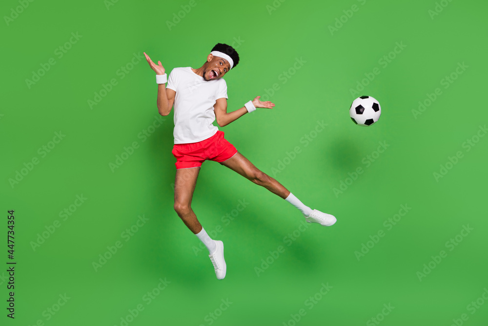 Photo of funky active guy jump kick ball wear headband white t-shirt shorts footwear isolated green color background