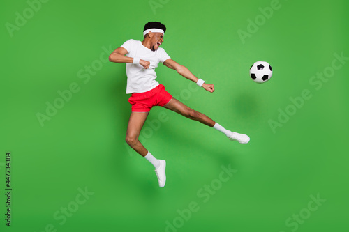 Fototapeta Naklejka Na Ścianę i Meble -  Full length photo of funky strong dark skin guy dressed sport outfit jumping playing football isolated green color background