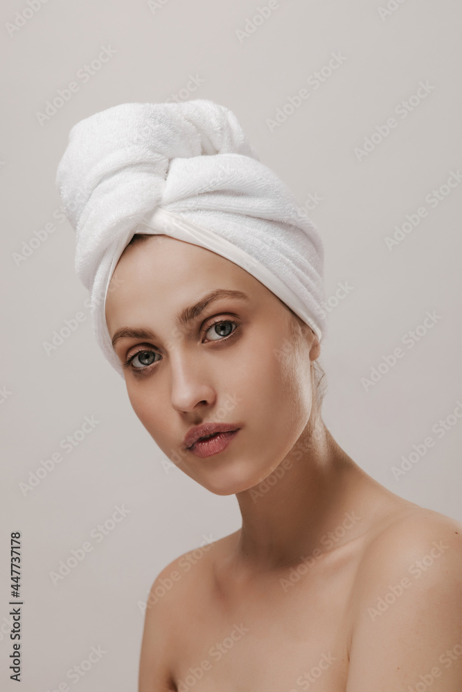 Engaging young lady with white towel on head, pure skin and naked shoulders, posing against light background. Beauty and wellness concept Engaging young lady with white towel on head, pure skin and naked shoulders, posing against light background. Beauty and wellness concept