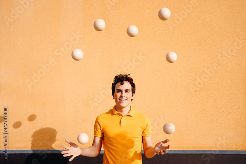 Agile man juggling balls near colorful wall