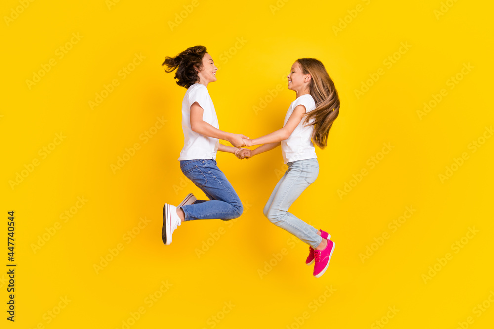 Full length body size view of two nice cheerful carefree kids jumping holding hands isolated over bright yellow color background