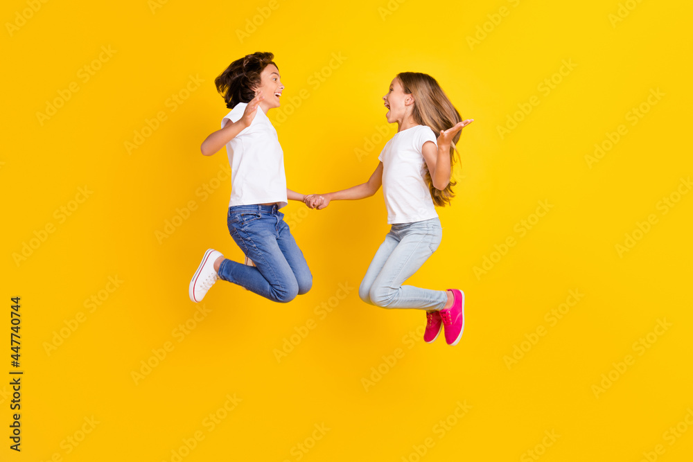 Full length body size view of two nice cheerful ecstatic kids jumping having fun rejoicing isolated over bright yellow color background Full length body size view of two nice cheerful ecstatic kids jumping having fun rejoicing isolated over bright yellow color background
