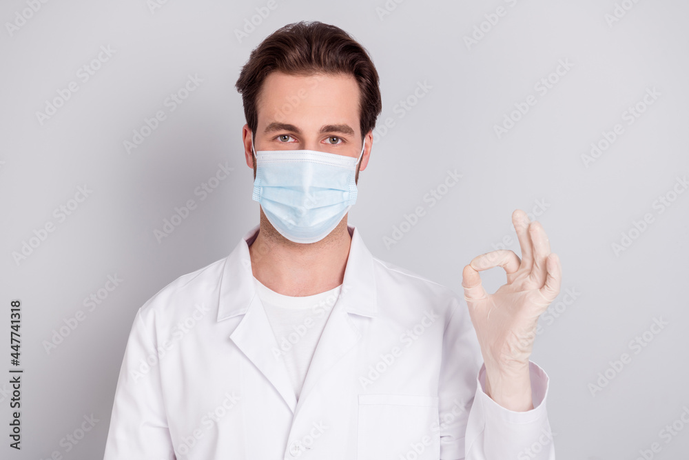 Photo of serious confident young guy doctor workwear showing okey sign isolated grey color background Photo of serious confident young guy doctor workwear showing okey sign isolated grey color background