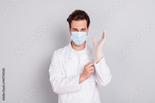 Photo of positive confident young doc man dressed white coat ready for operation put on glove isolated grey color background © deagreez