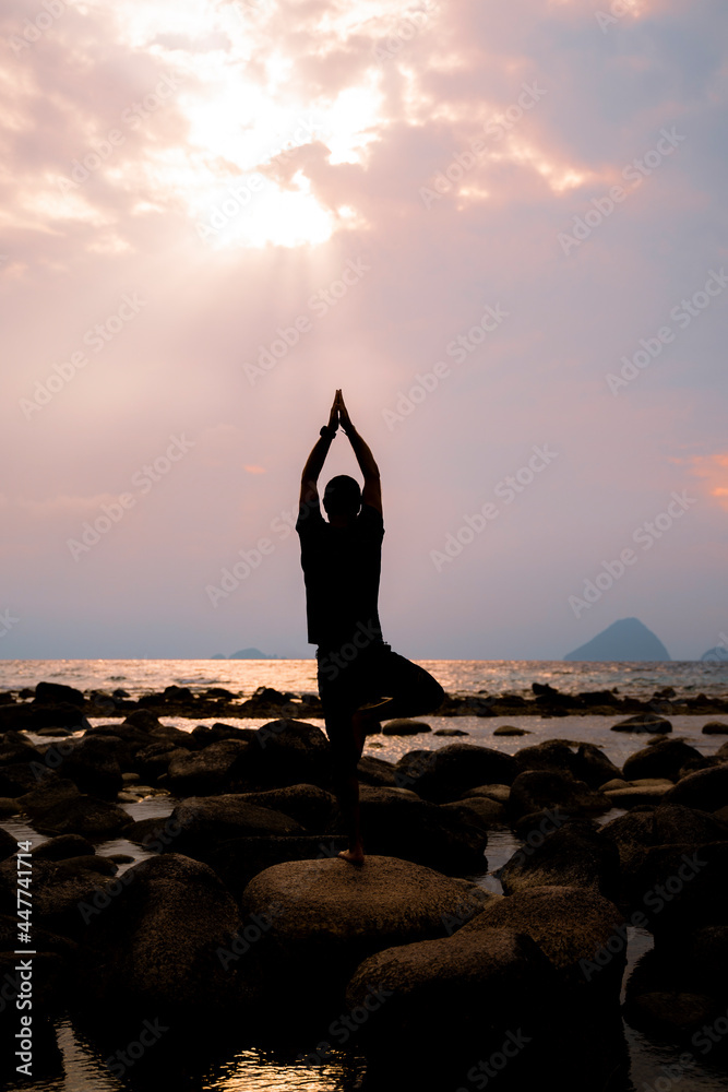 Man practicing yoga by the ocean at sunset