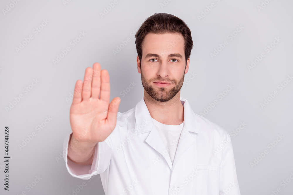 Photo of confident serious young doc man dressed white coat asking stop rising palm isolated grey color background Photo of confident serious young doc man dressed white coat asking stop rising palm isolated grey color background
