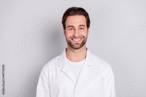 Photo of confident cheerful young guy doctor workwear smiling isolated grey color background © deagreez