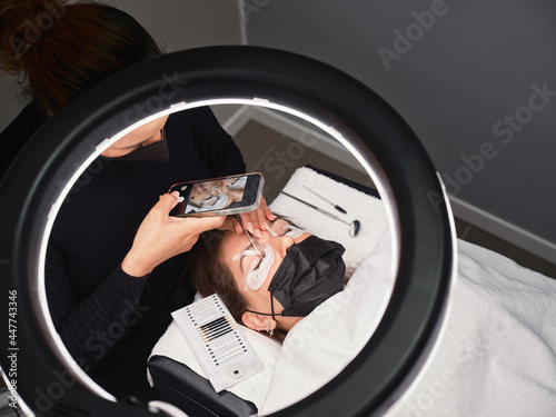 Beautician taking photo of client during eyelashes treatment procedure photo