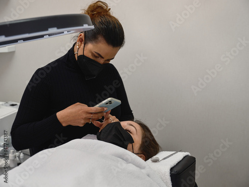 Beautician taking photo of client during eyelashes treatment procedure photo