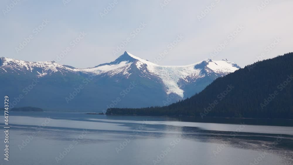 The mountain with green trees. In the background is a mountain with snow. The fjords of Alaska, unique natural landscapes. Alaska, USA. June 2019. The mountain with green trees. In the background is a mountain with snow. The fjords of Alaska, unique natural landscapes. Alaska, USA. June 2019.