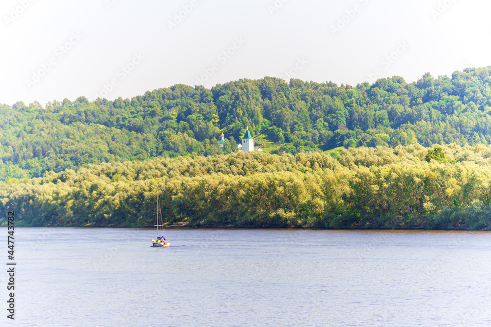A yacht is sailing along the river on a sunny day, a church is on the opposite bank
