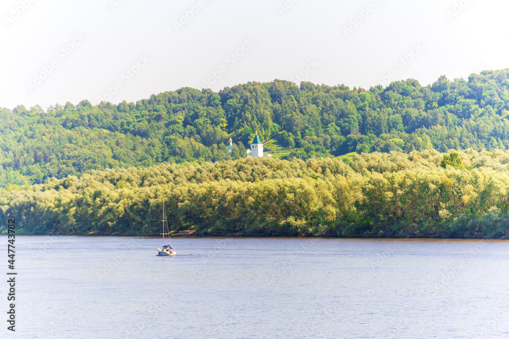 A yacht is sailing along the river on a sunny day, a church is on the opposite bank A yacht is sailing along the river on a sunny day, a church is on the opposite bank