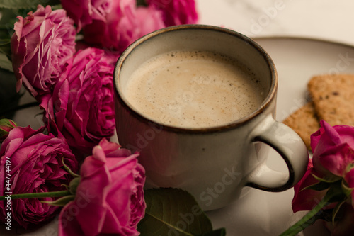 Coffee with milk in a blue ceramic mug, pink roses next to it. Gentle postcard of morning romantic breakfast with coffee.