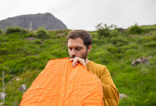 Young and attractive man inflating a mattress next to his tent to do solo camping in Scotland. Equipment to travel during vacation