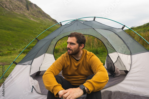 Obraz na płótnie Young and attractive man sitting on his tent set up outdoors enjoying nature in Scotland while doing solo camping w salonie