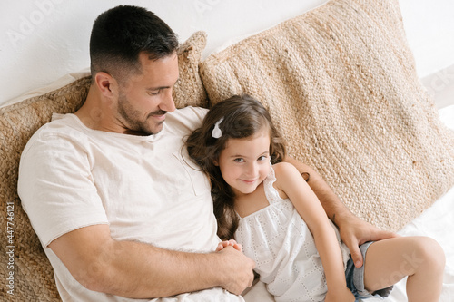 Loving father sitting with little daughter on bed at home