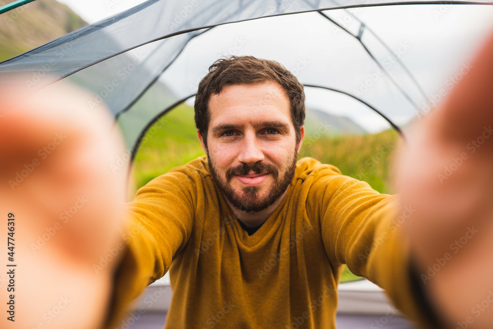 Photo of a young and attractive man taking a selfie inside a tent outdoors. Happy to do solo camping