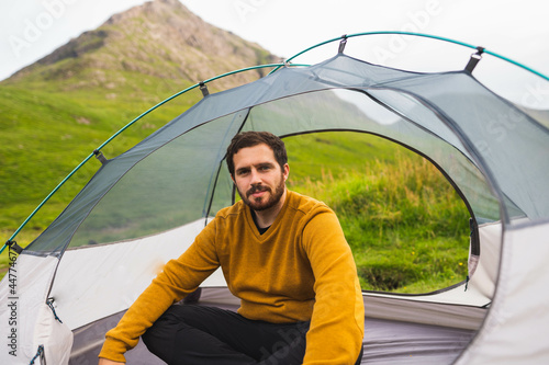 Obraz na płótnie Young and attractive man sitting on his tent set up outdoors enjoying nature in Scotland while doing solo camping w salonie