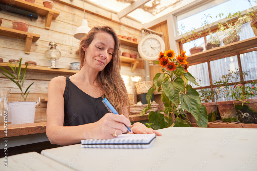 Smiling woman taking notes in notebook in glasshouse Smiling woman taking notes in notebook in glasshouse