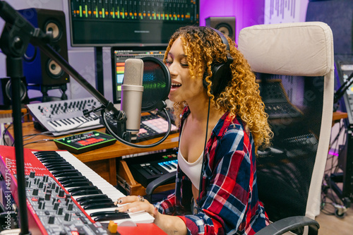 Black vocalist playing synthesizer while singing into microphone in studio