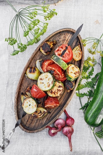 Vegetables kebab. Zucchini, tomatoes and sweet onions on a wooden platter. Grilled vegetables. Cooked vegetables and sauce. Food still life. Top view. Copy space