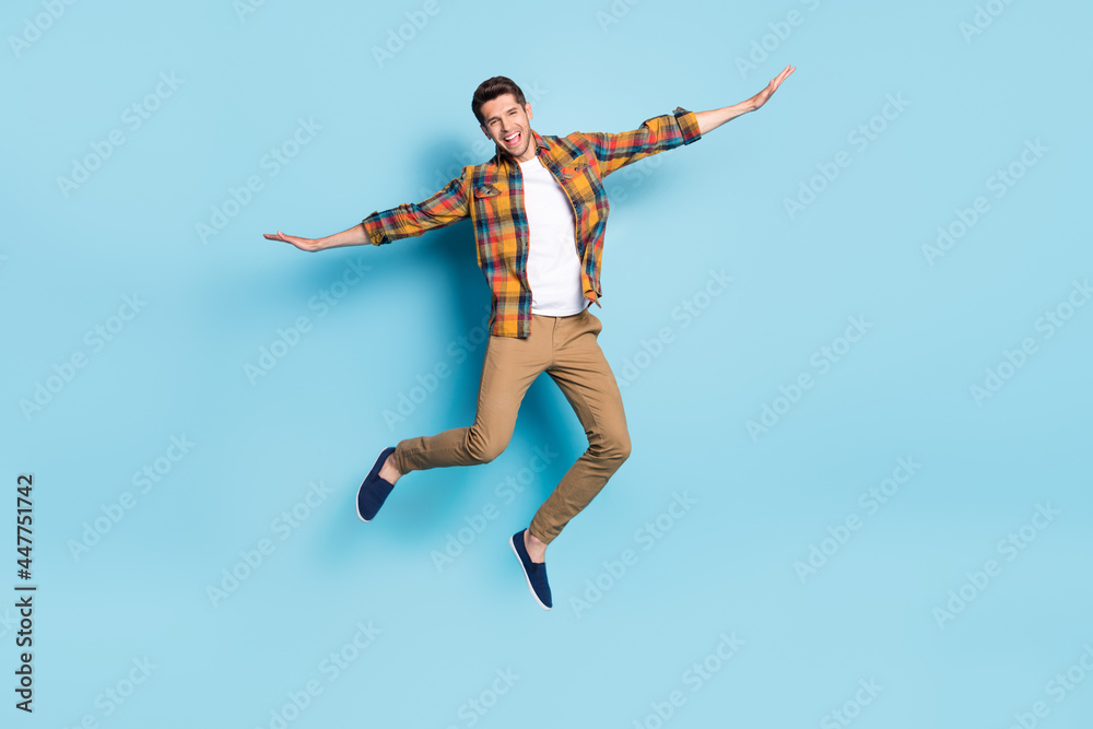 Photo of funny pretty young guy dressed plaid shirt spectacles smiling jumping high isolated blue color background