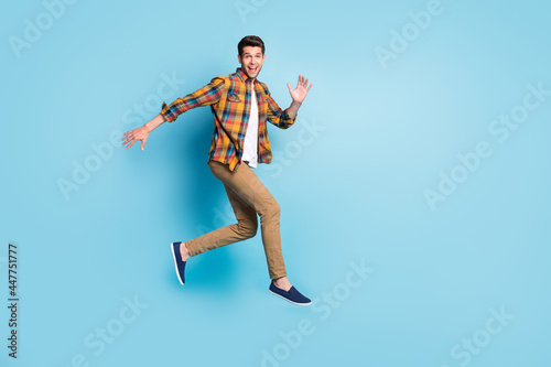 Photo of sweet excited young guy dressed plaid shirt spectacles smiling jumping high isolated blue color background