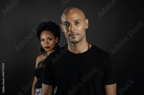  Bald man in foreground in focus and smiling afro girl in background on black background. Concept latin people 