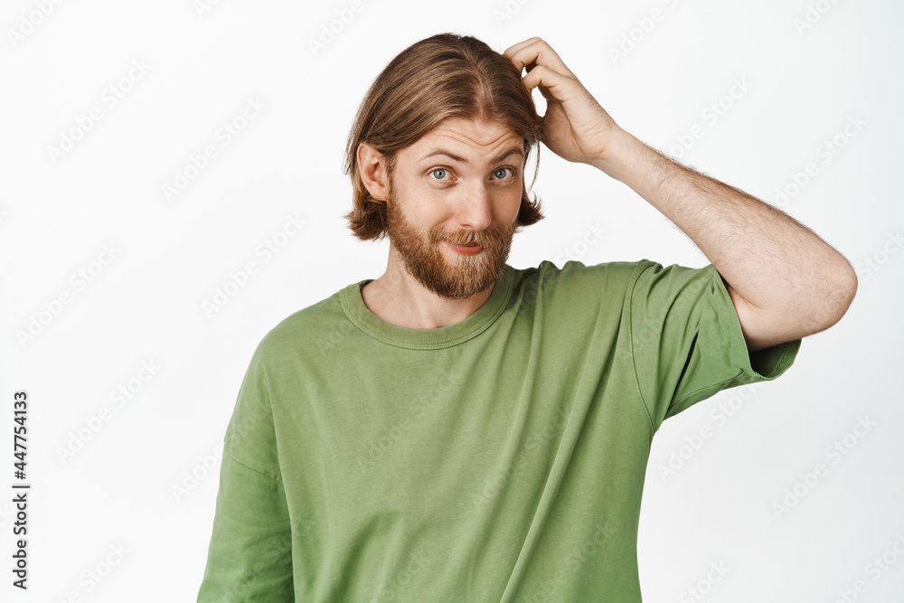 Image of handsome hipster guy, man with blond hair and beard, sratching his head and smiling clueless, standing in green t-shirt against white background Image of handsome hipster guy, man with blond hair and beard, sratching his head and smiling clueless, standing in green t-shirt against white background