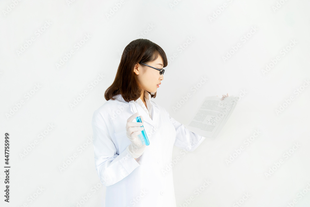1本の試験管を手に持ち技術資料を見ている若い女性技術者の横姿の上半身
