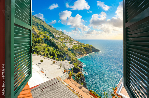 View through an open window with shutters of the ocean front hilltop town of Praiano, Italy, along the Amalfi Coast.