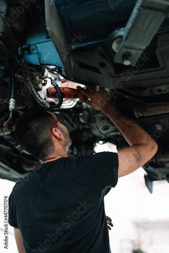 Car mechanic repair car suspension of lifted automobile at repair service station