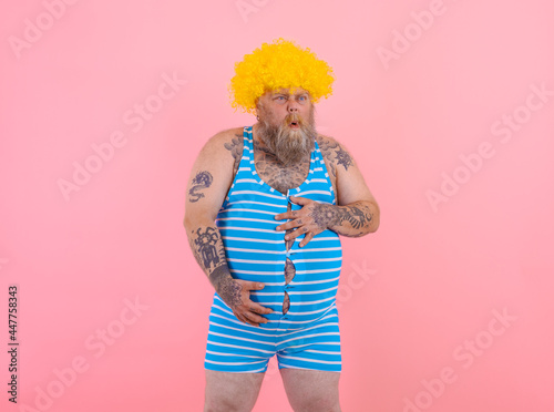 Slika na platnu Happy man with yellow wig and swimsuit has stomachache