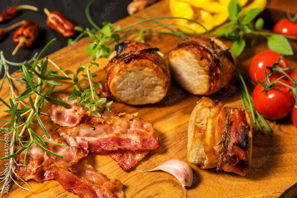 Fototapeta premium Grilled pork medallions with herbs and spices. Pork tenderloin with bacon. Grilled meat and tomatoes. Summer barbecue. Diet food.