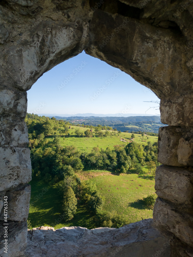 Panoramic hilly landscape of Srebrenik village with forests and meadows viewed through stone window of medieval ottoman fortress Srebrenik