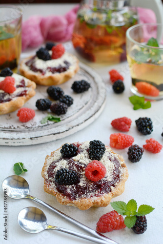 Sweet baskets with cream, raspberries and blackberries, herbal tea and mint leaves on a light background. Vertical