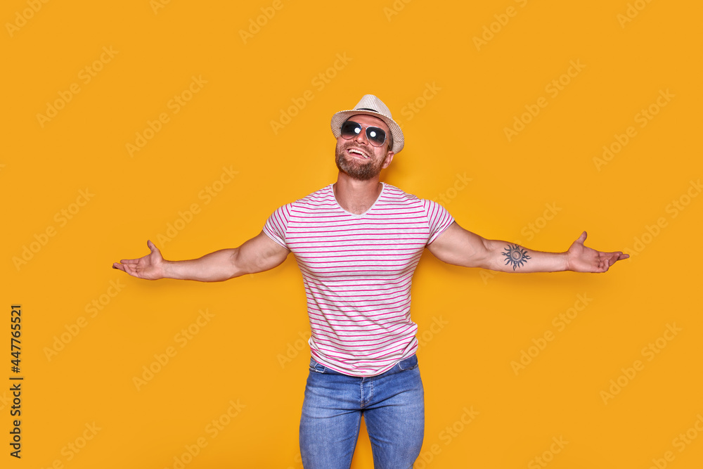 Surprised successful young man in sunglasses and summer straw hat screaming with hands wide open over yellow background Surprised successful young man in sunglasses and summer straw hat screaming with hands wide open over yellow background