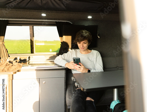 Photo of an attractive young female using her phone while sitting in a sofa inside of a campervan