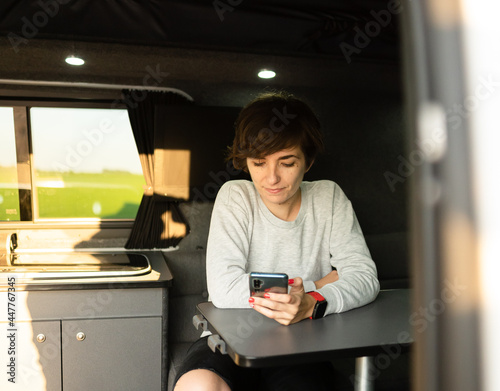 Photo of an attractive young female using her phone while sitting in a sofa inside of a campervan