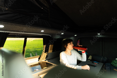 Photo of an attractive young female drinking water from a reusable bottle while sitting in a sofa inside of a campervan