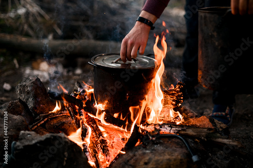 man's hand holds the lid of saucepan that stands on burning fire