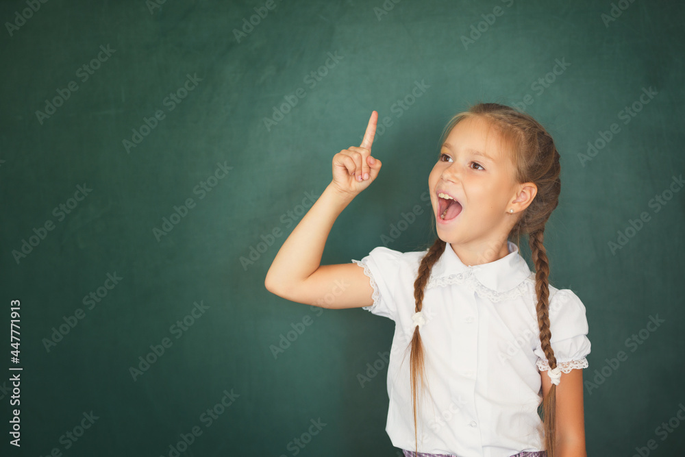 Smiling young little child girl in school on blackboard background. Education and school concept