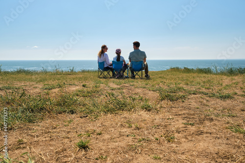 Parents and their kid sitting together at capmsite outdoors.