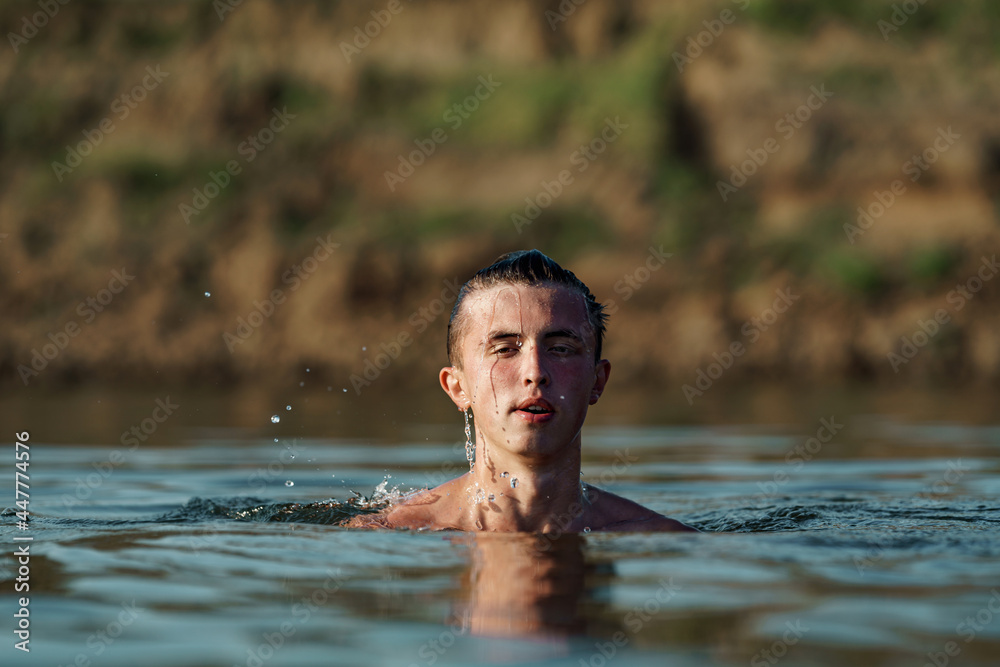 young attractive man swims in a river or lake, in deep dangerous water.The freshness of the wild nature. Relaxation and active summer vacation. Swimming skills. Dive into the water