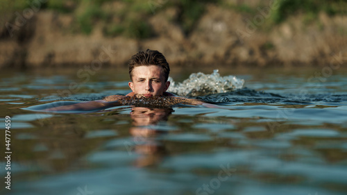 Fototapeta Naklejka Na Ścianę i Meble -  young attractive man swims in a river or lake, in deep dangerous water.The freshness of the wild nature. Relaxation and active summer vacation. Swimming skills. Dive into the water