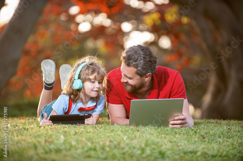 dad and son use laptop for video call or lesson listen music in headphones in park, education online © Olena