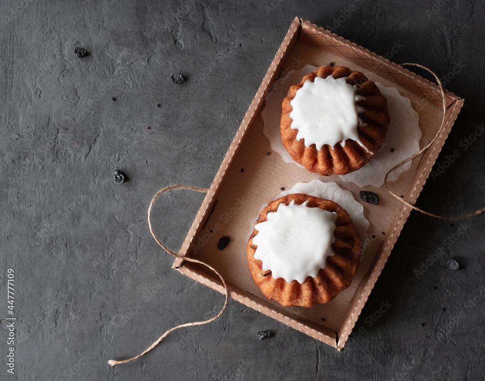 Rum baba cake. Two rum buns with raisins and white glaze in a box on a