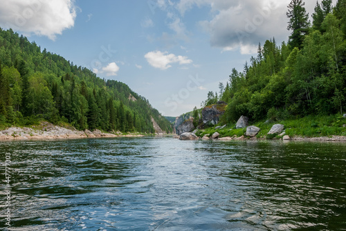 Landscape of Siberia. Kiya River, mountain banks and green forests in the Kemerovo region. Daytime landscape with blue skies and clouds.