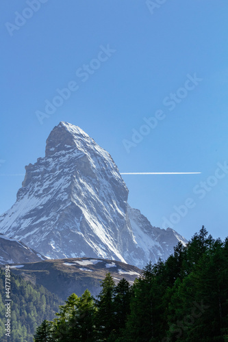 View of iconic Matterhorn mountain summit with snow from Zermatt valley, with green vegetation, trees and wooden cottages, Valais, Swiss Alps, Switzerland